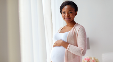 Pregnant woman standing with her hand on her belly smiling at the camera